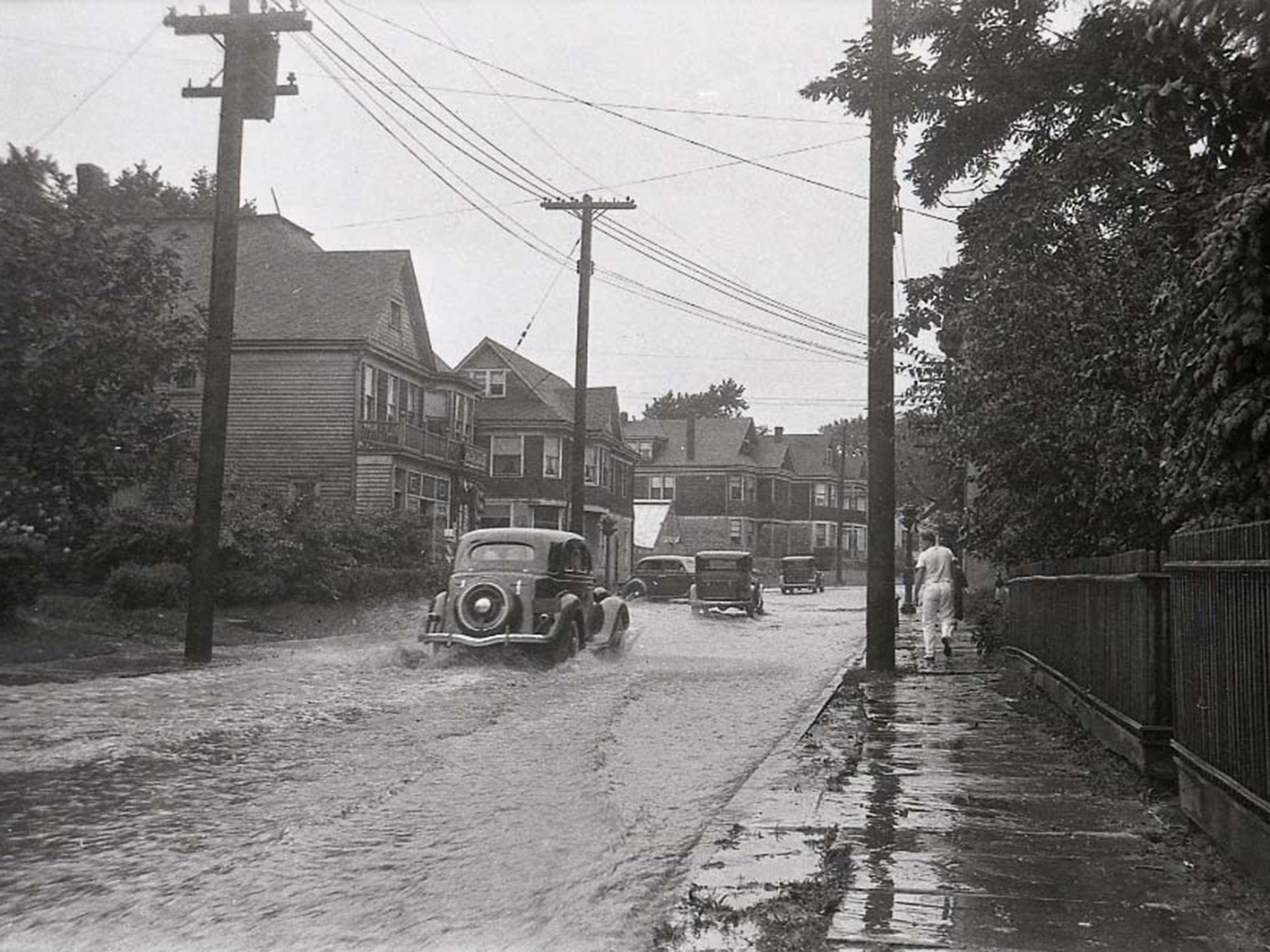 Vintage cars shown driving through a flooded street