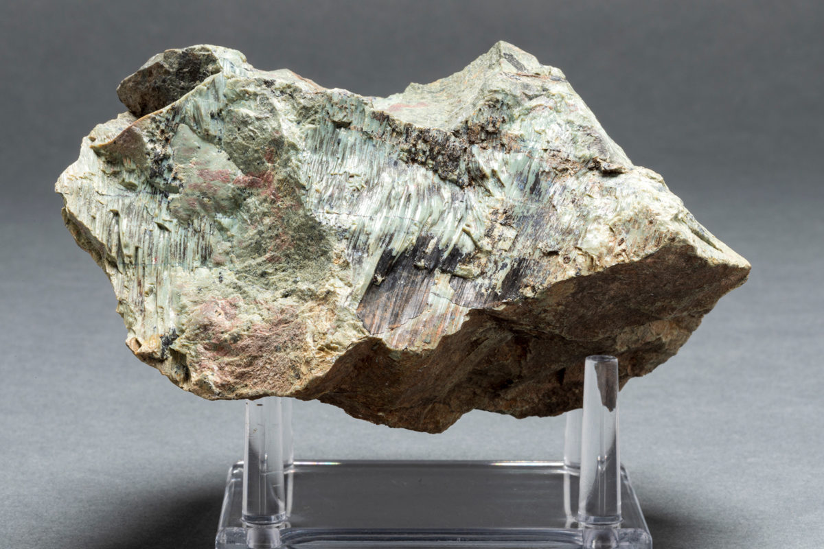 A piece of Serpentenite, a greenish rock, on a grey background