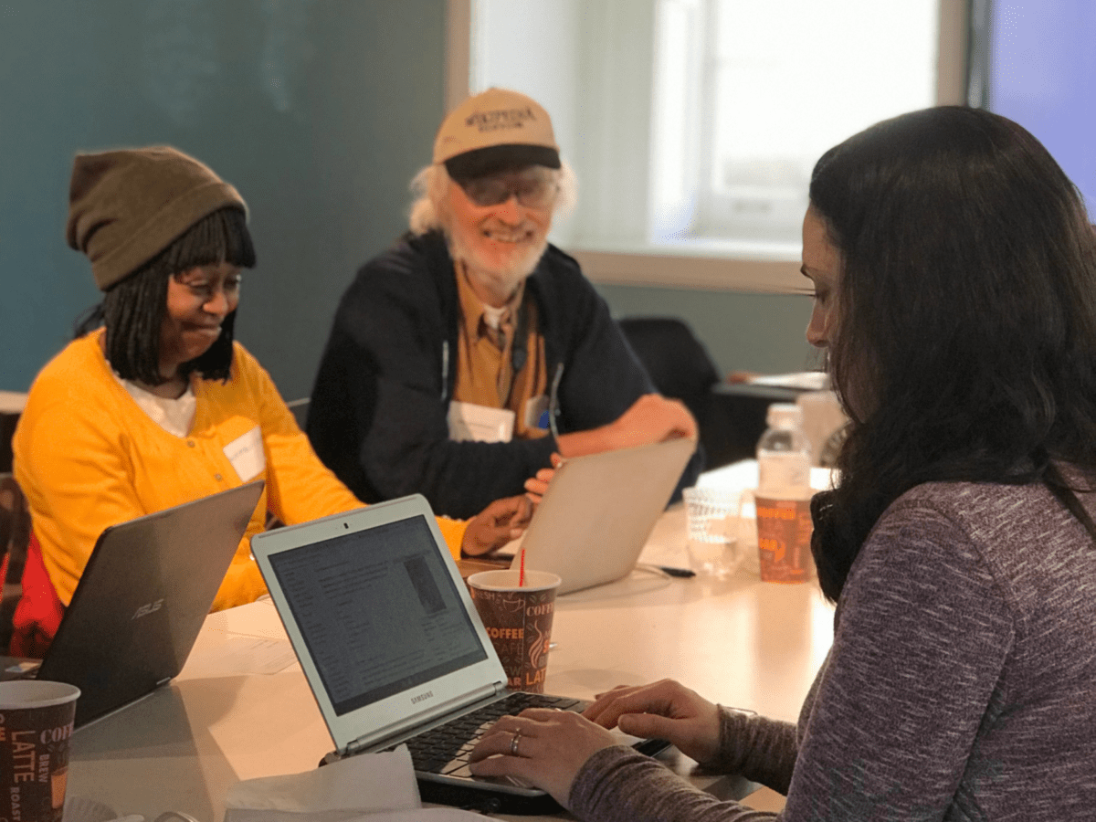 Three people sitting at a table in front of computers
