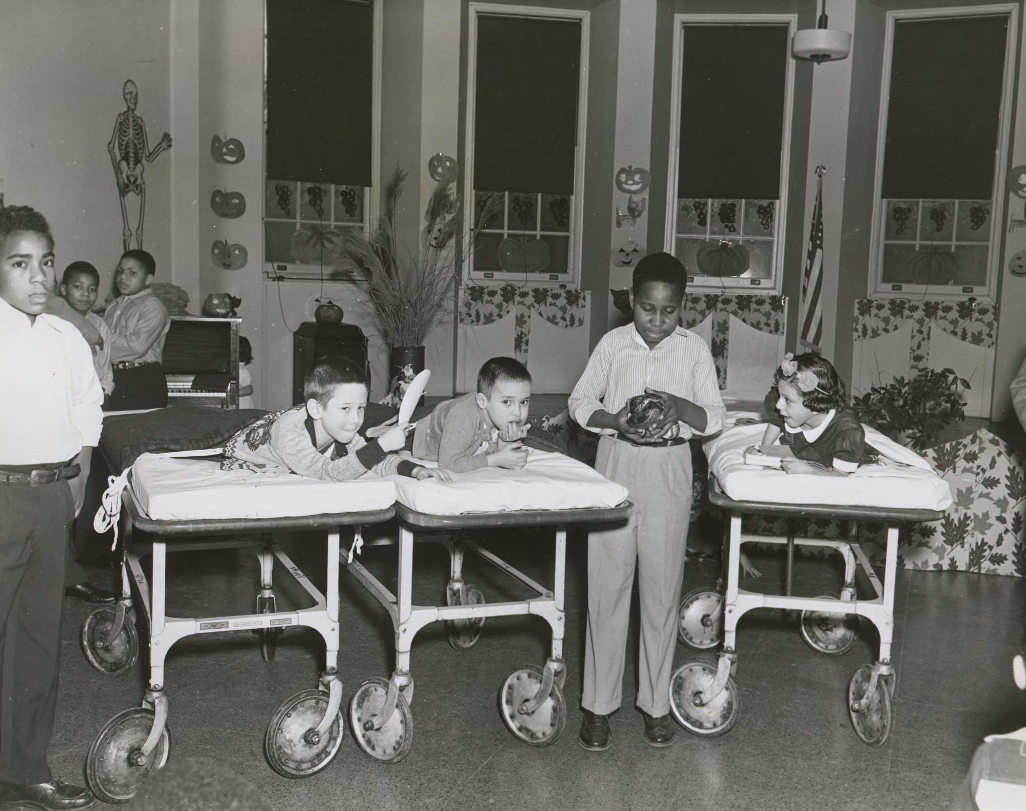 Photo of a boy standing between children on cots holding a snake