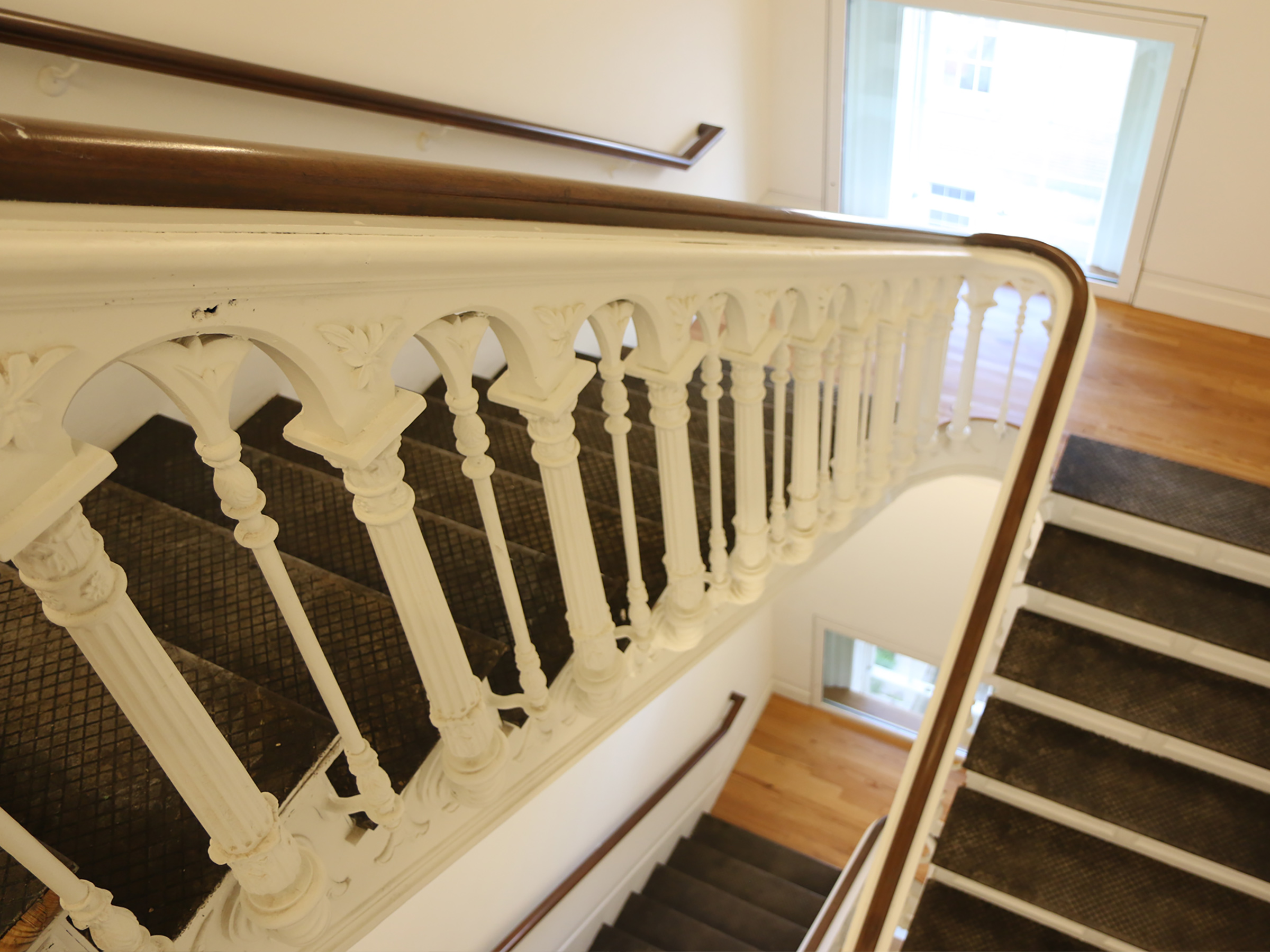 Photograph looking down a historic staircase with a brown banister and white balusters