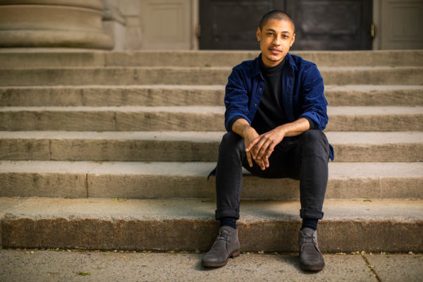 Photograph of James Vincent Brice sitting on stone steps wearing a navy blue button down shirt and black pants.