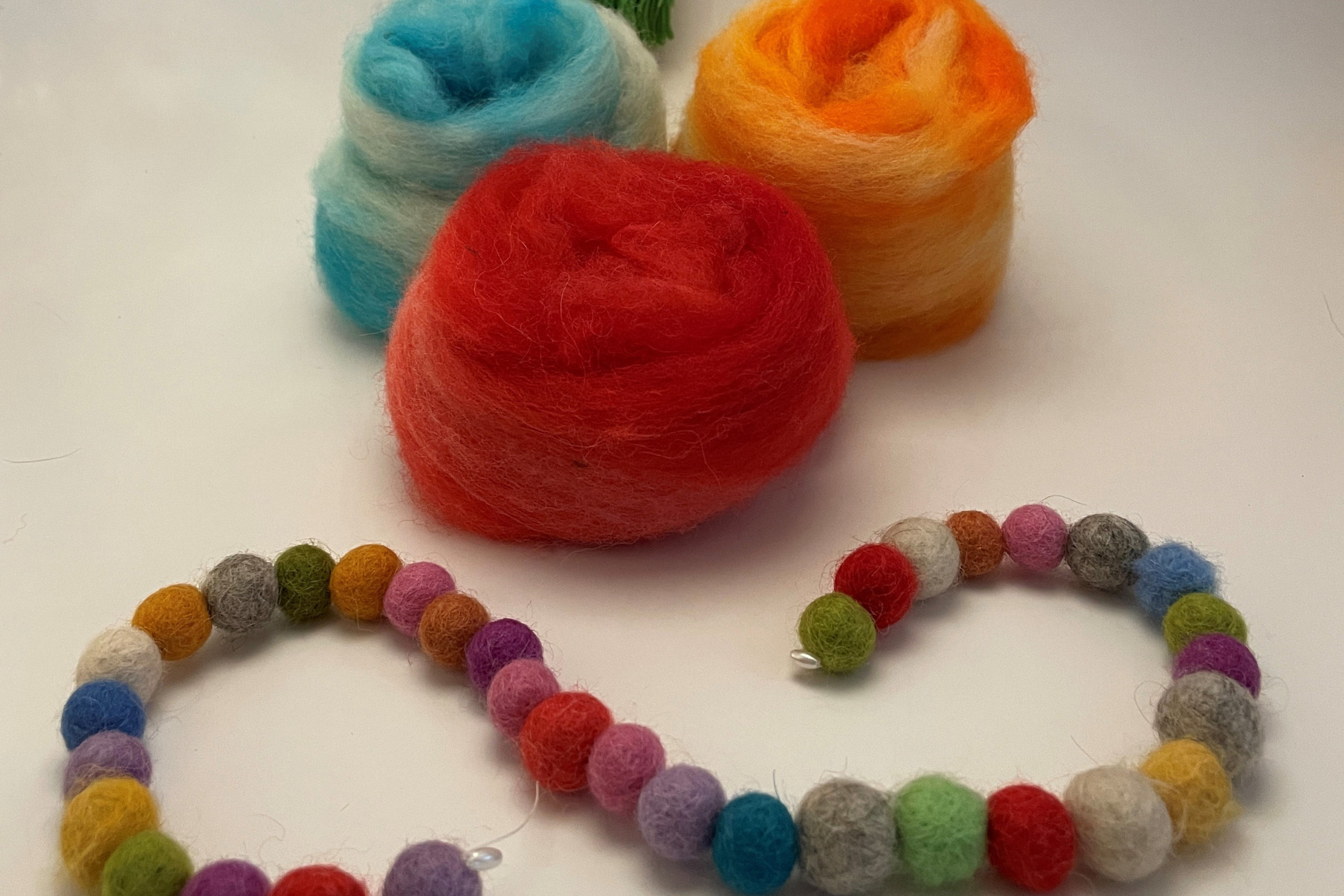Three felt balls blue, red, and orange with a string of smaller felt balls in front, multicolored