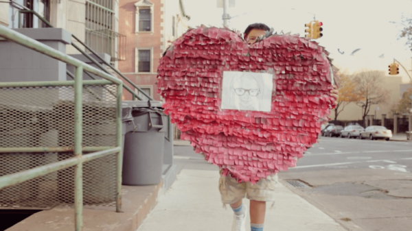 A child carrying a giant read heart piñata down a city street