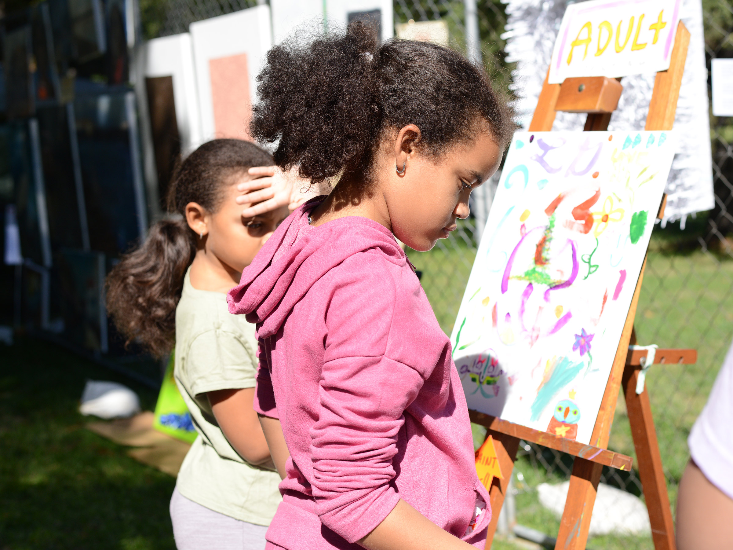 Two young girls painting outdoors on an easel.