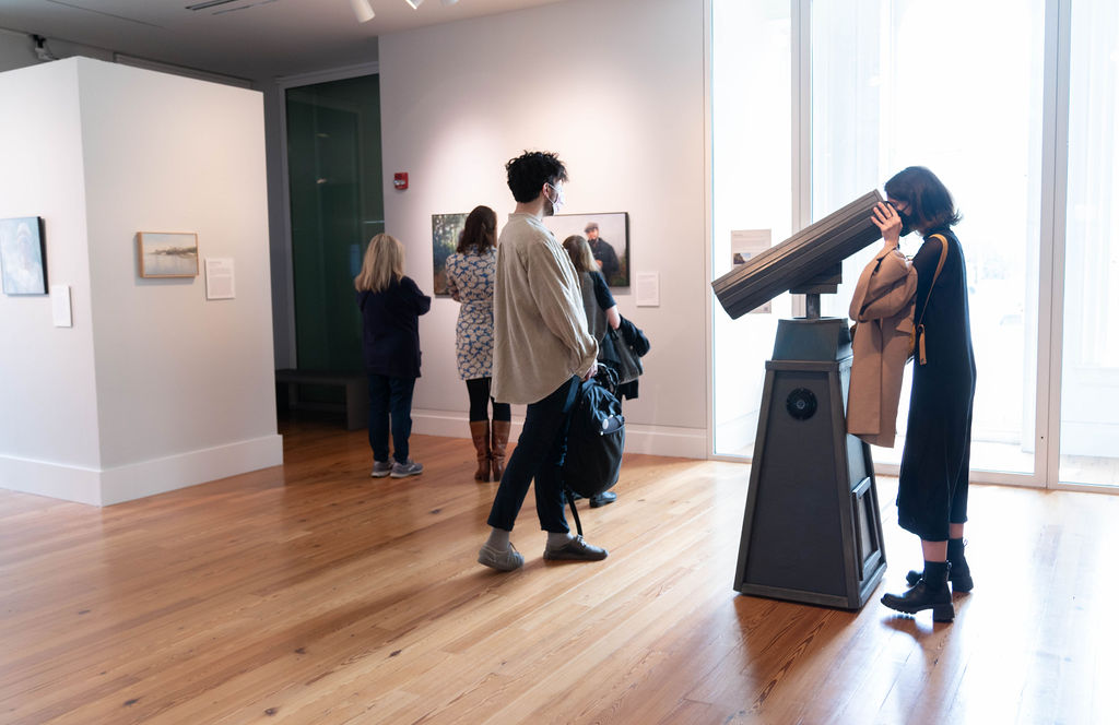 People in a gallery with a view finder at the center with someone looking through
